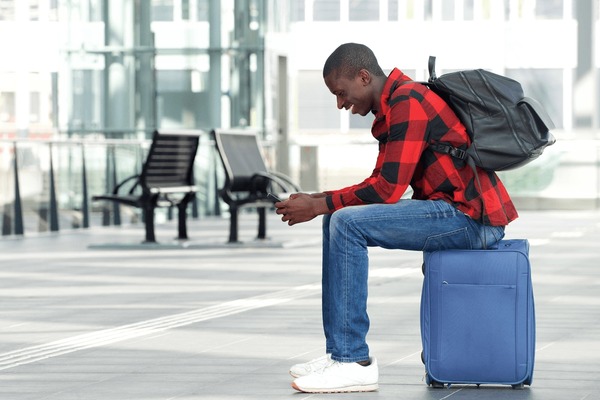 Side,portrait,of,happy,young,man,sitting,on,traveling,bag